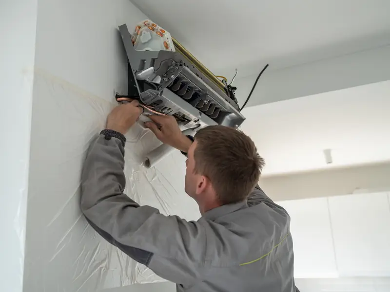 Installateur fixant un split mural dans la pièce principale d'un appartement