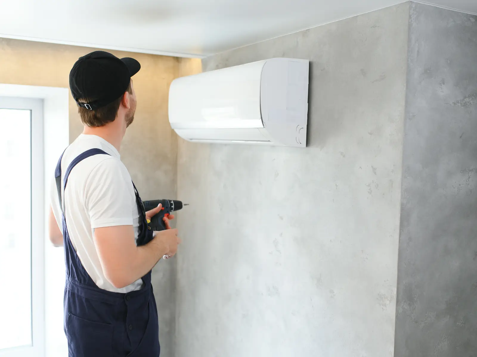 Technicien fixant une unité murale de climatisation lors d'une pose