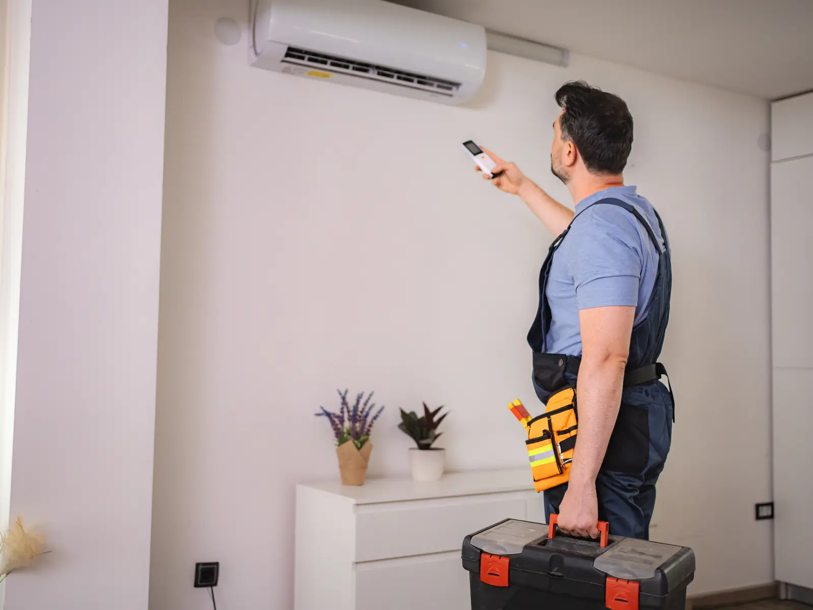 Technicien testant une climatisation murale à la télécommande après la réparation d'un défaut